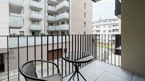 A balcony with a glass table and two chairs, overlooking a residential area with multi-story buildings.