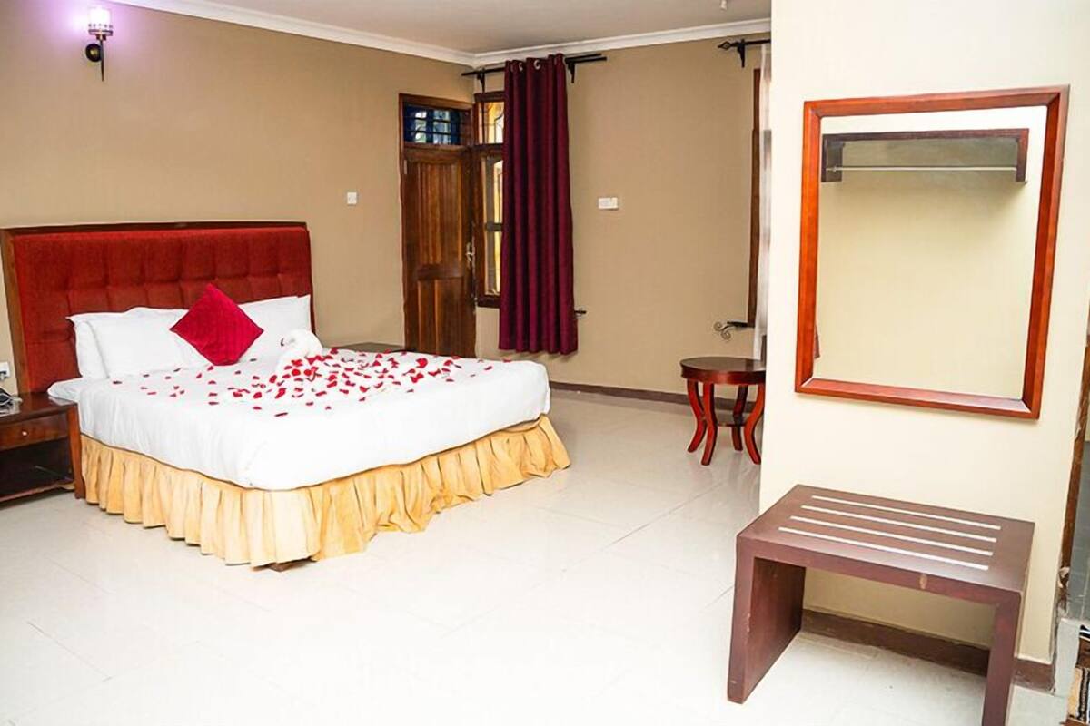 Ein Hotelzimmer mit einem großen Bett, einem Nachttisch, einem kleinen Tisch, einem Spiegel und einer Bank.