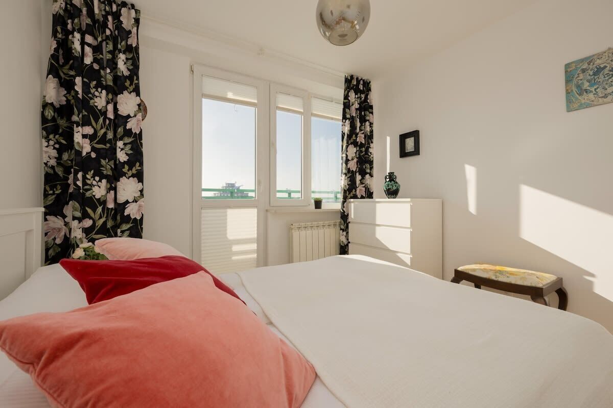 Une chambre à coucher avec un lit, une fenêtre, un radiateur, une petite table et un tableau accroché au mur.