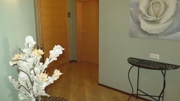 Un pasillo con puertas de madera, un cuadro de rosa colgado en la pared, una cesta de mimbre y una mesa de metal.