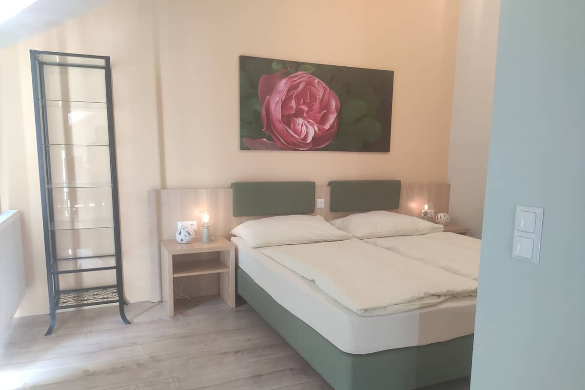 A bedroom with a bed, nightstands, a wall-mounted picture, and a wooden floor.