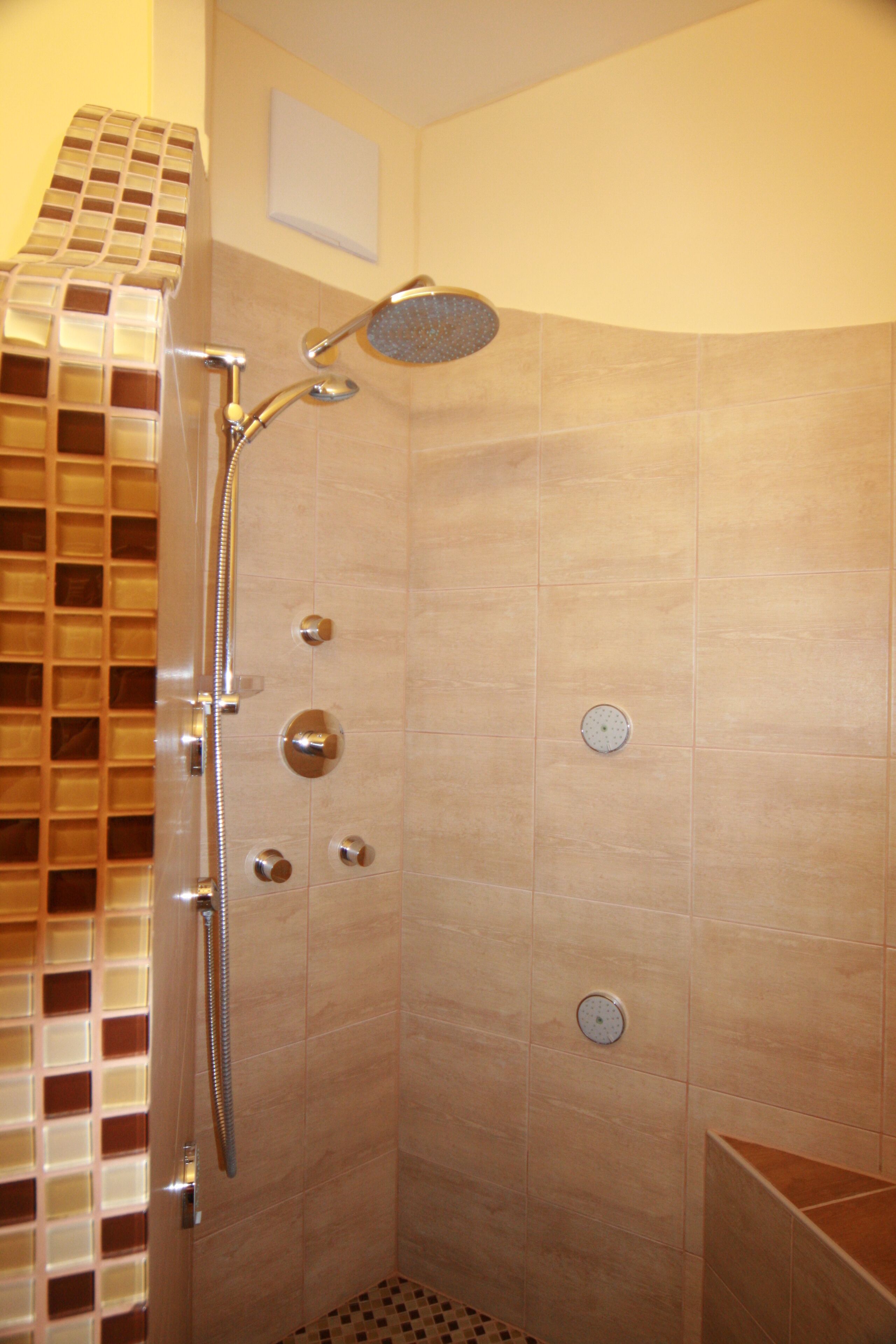 A shower with a handheld showerhead, a wall-mounted control panel, and a tiled floor.