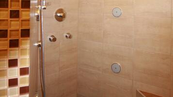 A shower with a handheld showerhead, a wall-mounted control panel, and a tiled floor.