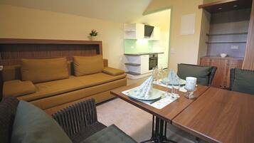 A compact living space with a sofa, a dining table set with plates and glasses, and a kitchenette in the background.