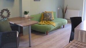 Una sala moderna con un sofá verde, una mesa de madera y un sillón verde. Se observan estantes en la pared con objetos decorativos y un radiador.