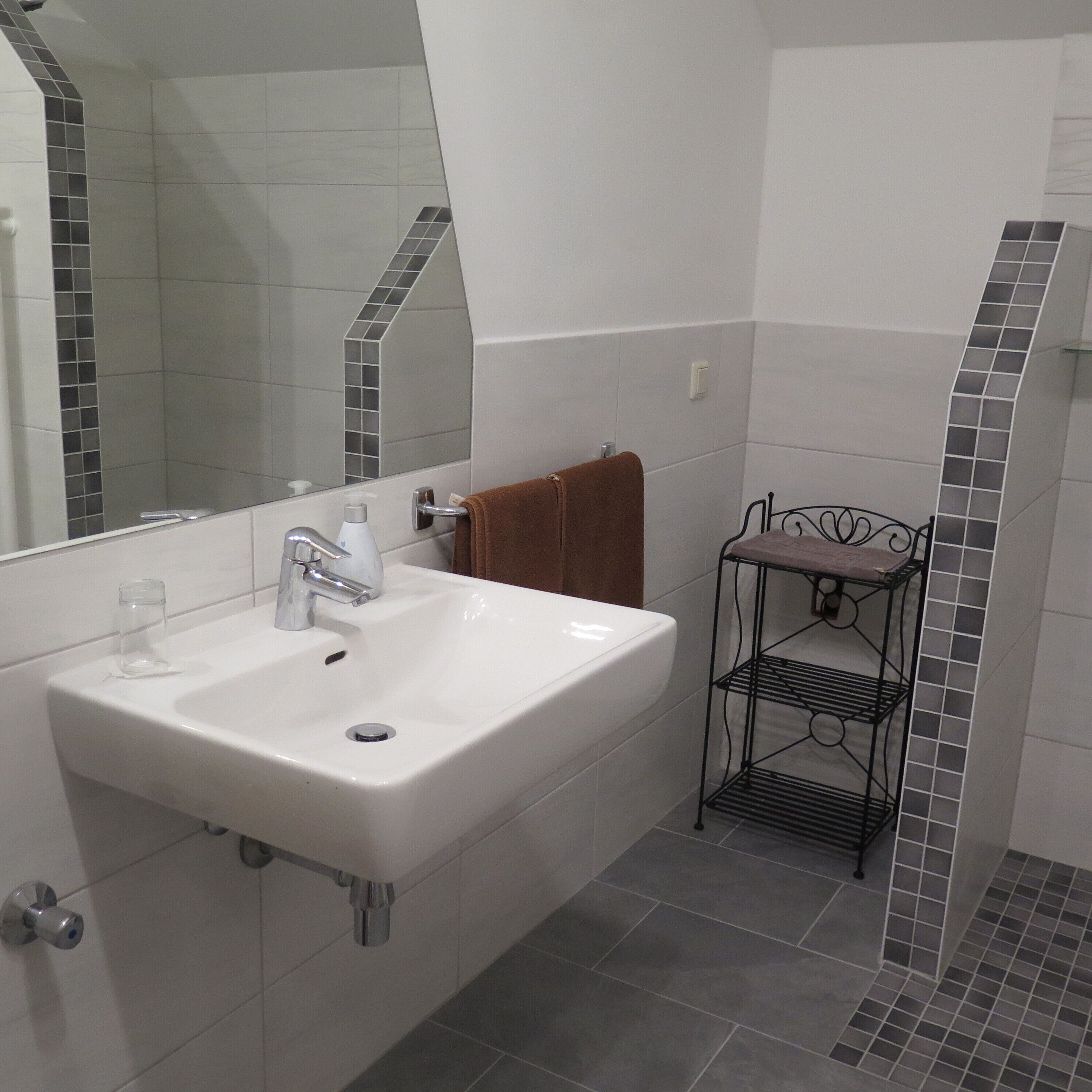 A bathroom with a white sink, a mirror, and a metal shelf.