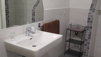 A bathroom with a white sink, a mirror, and a metal shelf.