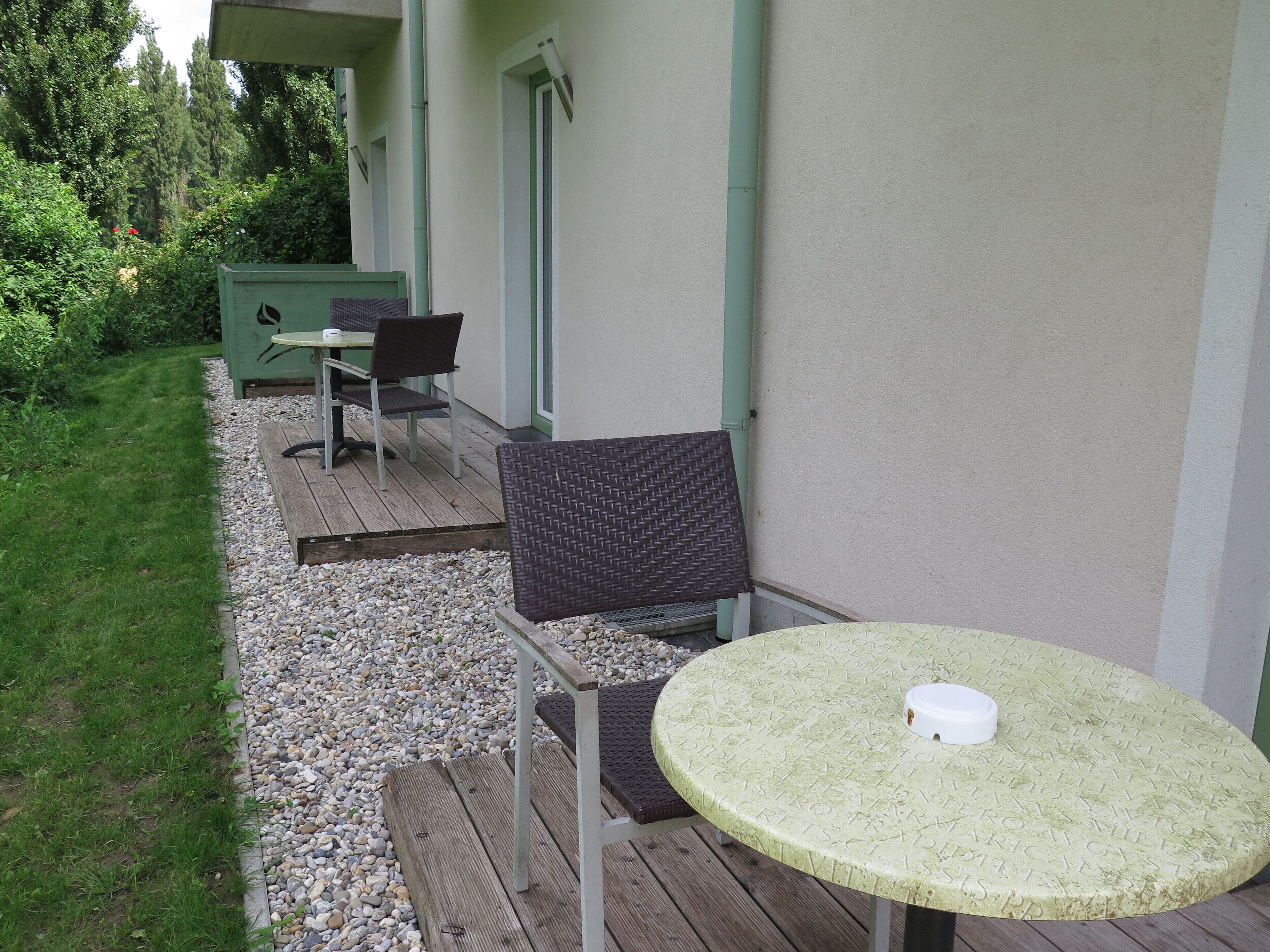 Eine Terrasse mit einem runden Tisch und zwei Stühlen, einem kleinen Tisch mit einem Stuhl und einem grünen Schrank.