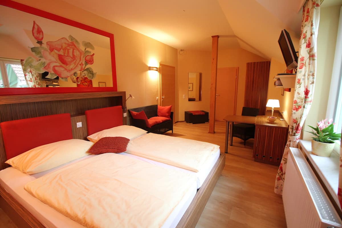 A hotel room with two beds, a desk, a chair, a TV, and a large floral painting on the wall.