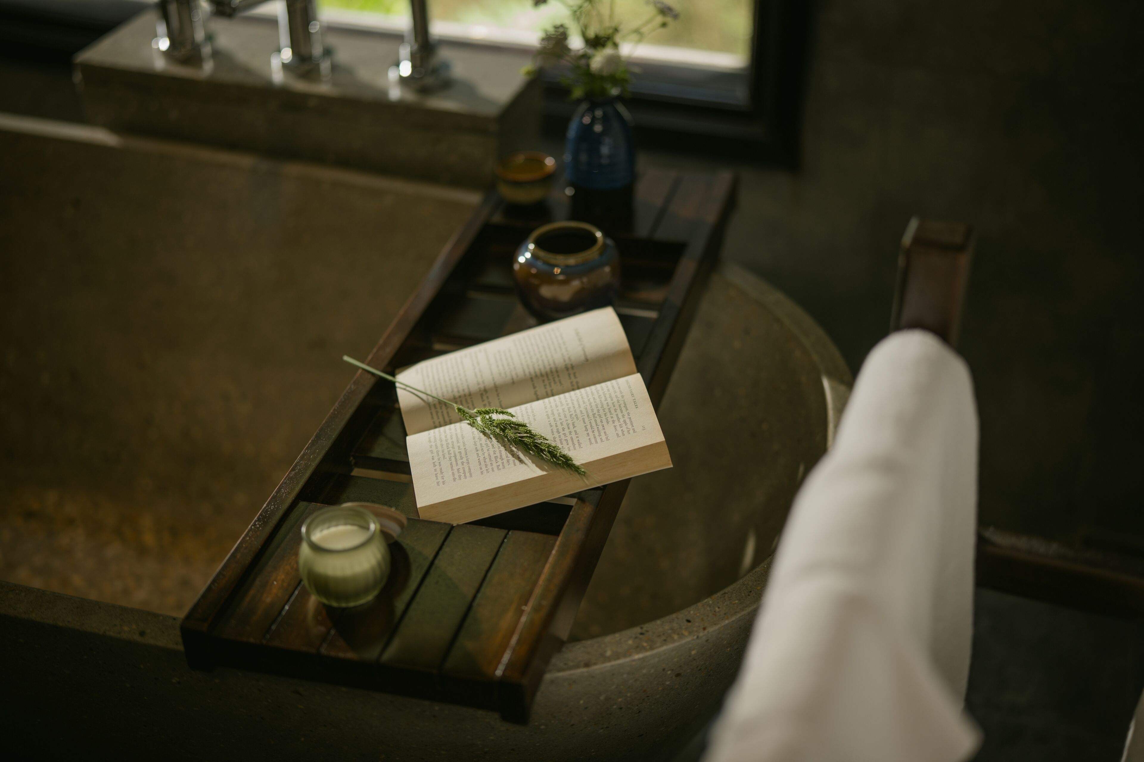 Een houten dienblad met een boek, een kaars en een kleine vaas op een stenen bank.