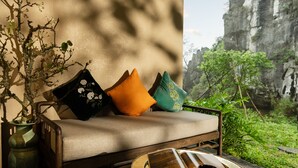 Ein Zimmer mit einer Couch, Kissen, einem Tisch mit einer Tasse und Blick auf Grünpflanzen und eine Felsformation.