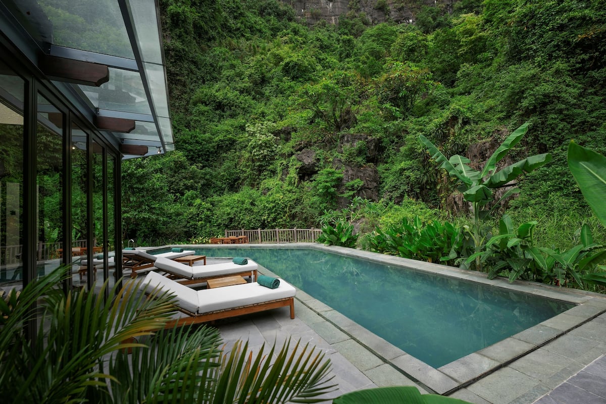 Zona de piscina con sillones de descanso y vistas a una ladera verde y exuberante.