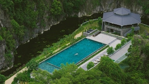 Eine Vogelperspektive auf einen Urlaubsort mit einem Swimmingpool, umgeben von üppiger Vegetation und einer Klippe.