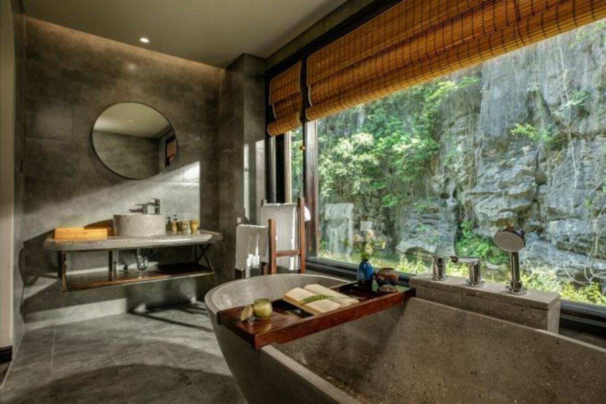 Een moderne badkamer met een groot bad, een ronde spiegel en een raam met uitzicht op een rotsachtig landschap.