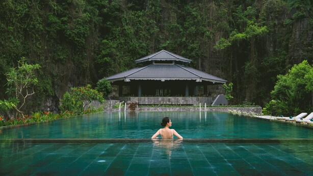 Eine Frau in einem Schwimmbecken, im Hintergrund ein traditionelles Gebäude.