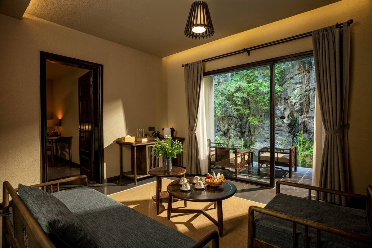 Una habitación con cama, una mesa de comedor con sillas, una pequeña cocina y un ventanal con cortinas.