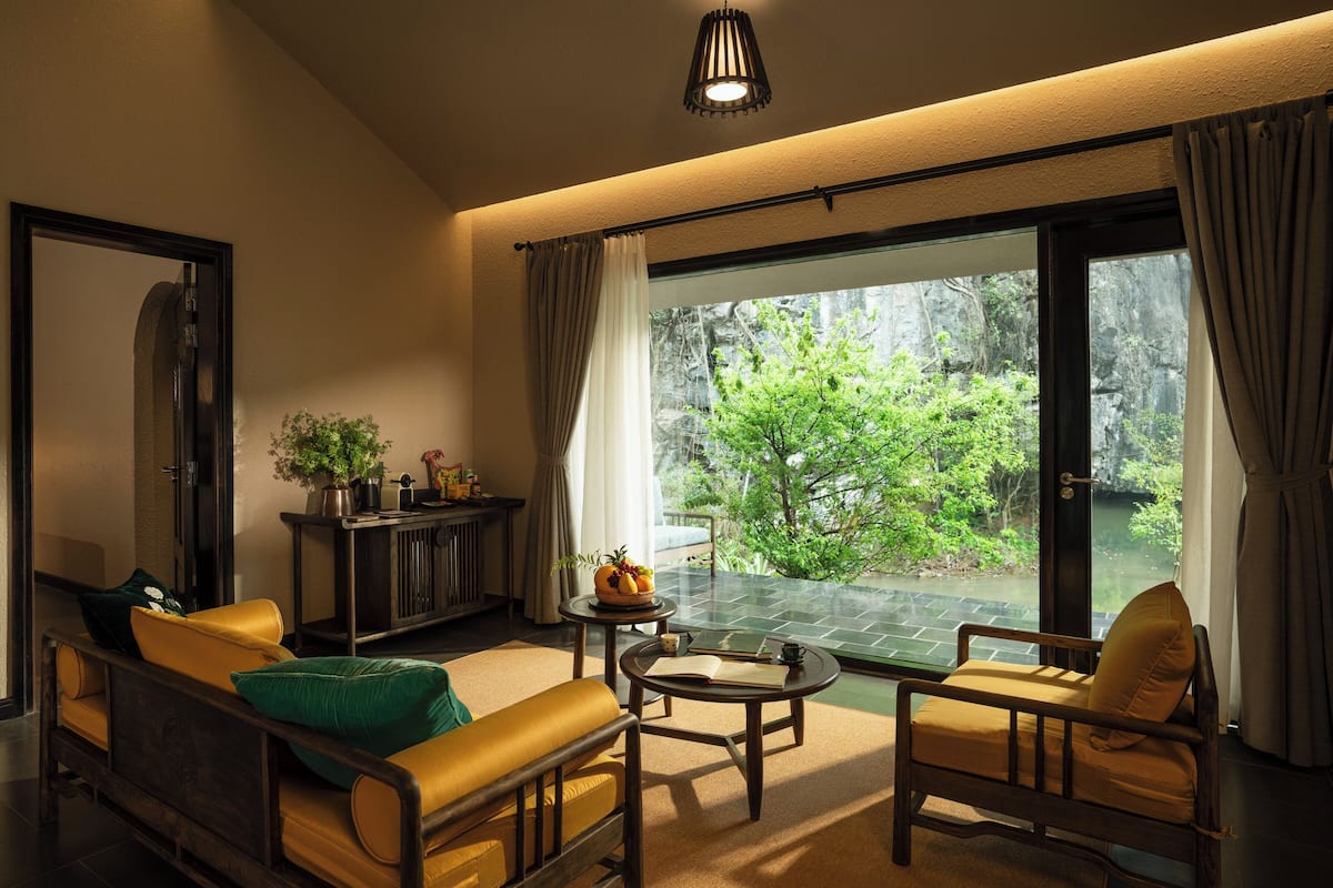 Una sala de estar moderna con un sofá, sillones, una mesa de centro y vistas a un jardín exuberante a través de amplios ventanales correderas.