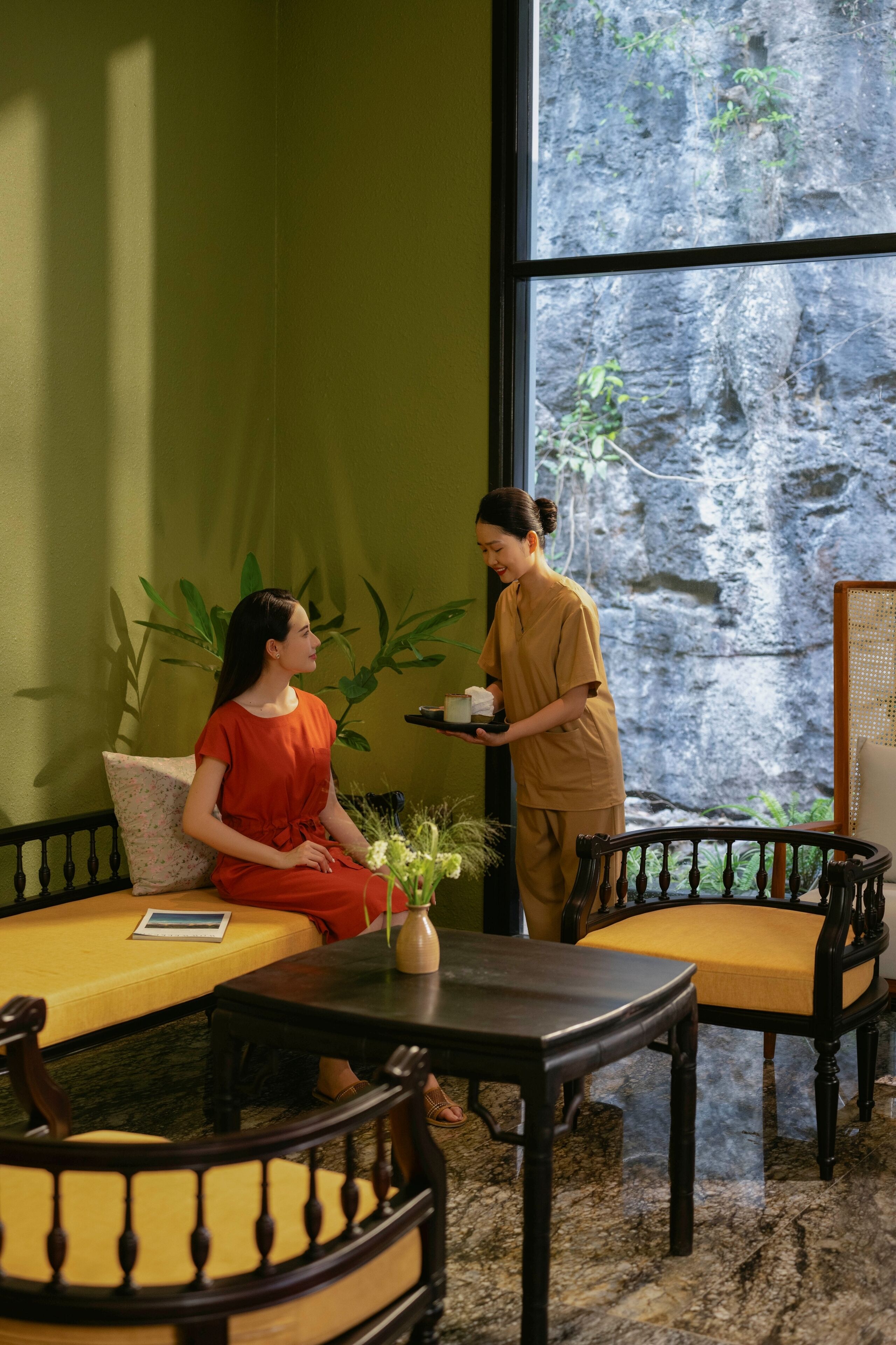 Una habitación con pared verde, un ventanal con vistas a un paisaje rocoso, un sofá, una mesa y una silla.