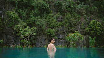 Una persona en una piscina cristalina con un risco rocoso y abundante vegetación al fondo.