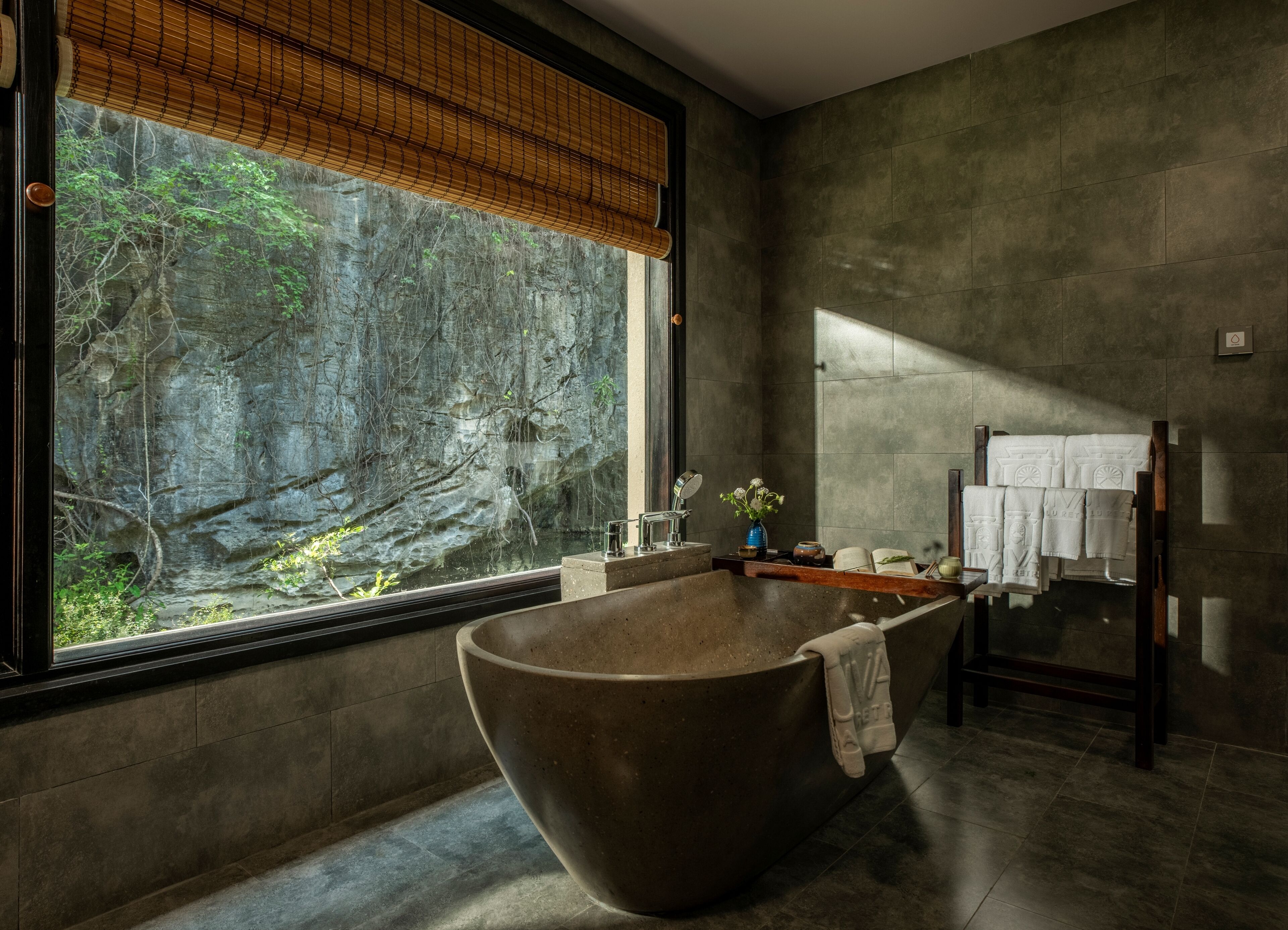 A modern bathroom with a freestanding bathtub, a large window with a view of a rocky landscape, and a towel rack with multiple towels.