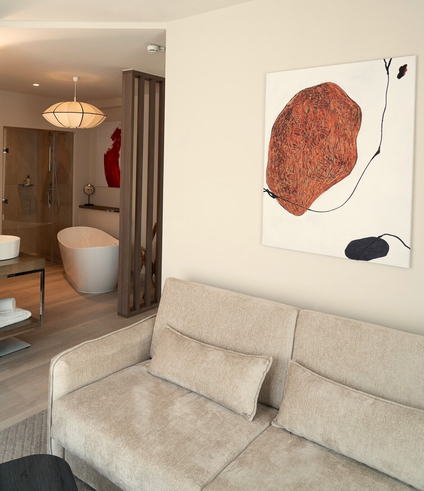 A modern living room with a beige sofa, a glass shower enclosure, and a large abstract painting on the wall.