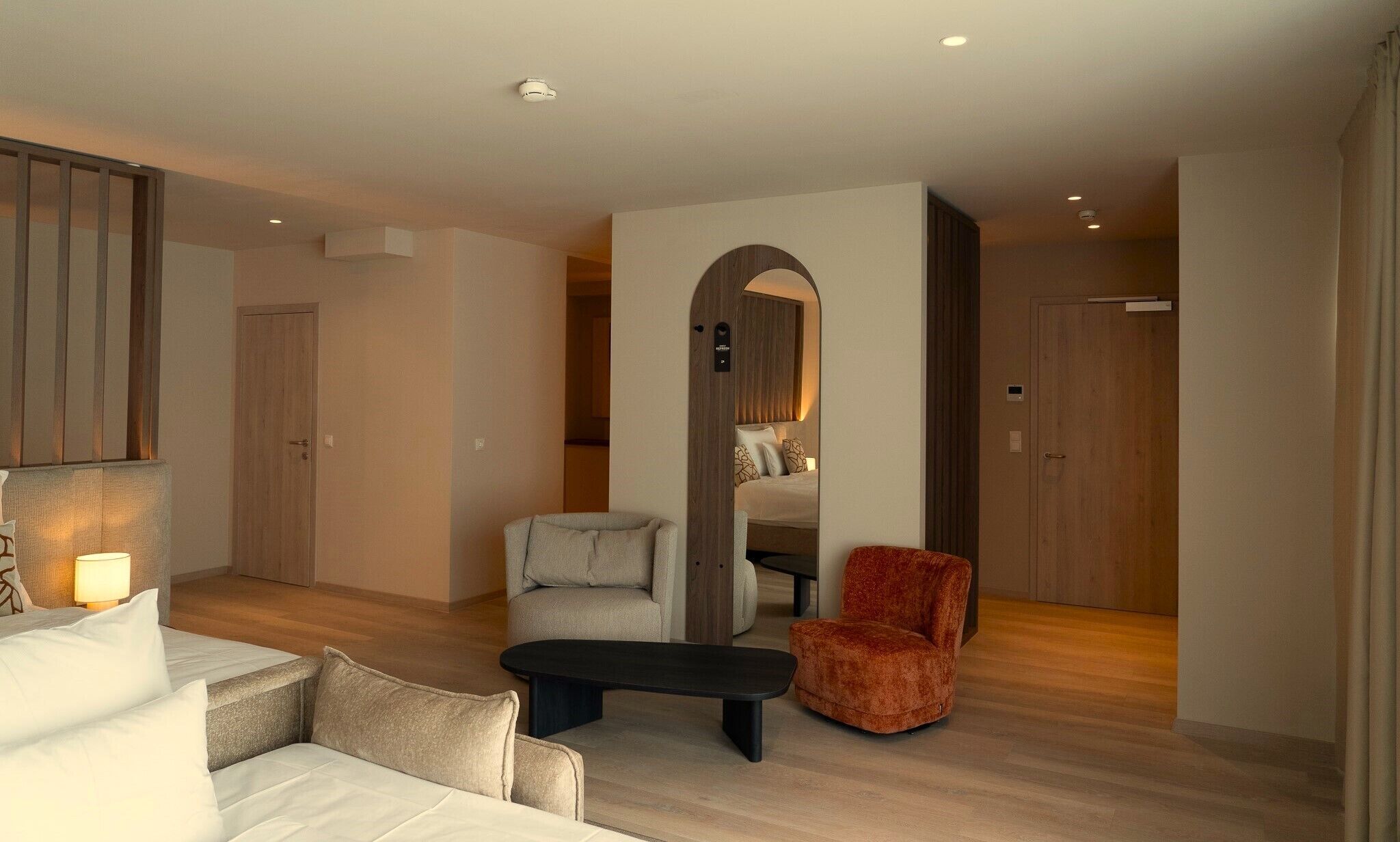 Ein modernes Hotelzimmer mit einer Couch, einem kleinen Tisch, einem roten Sessel und einem Bett mit einem Holz-Kopfteil.