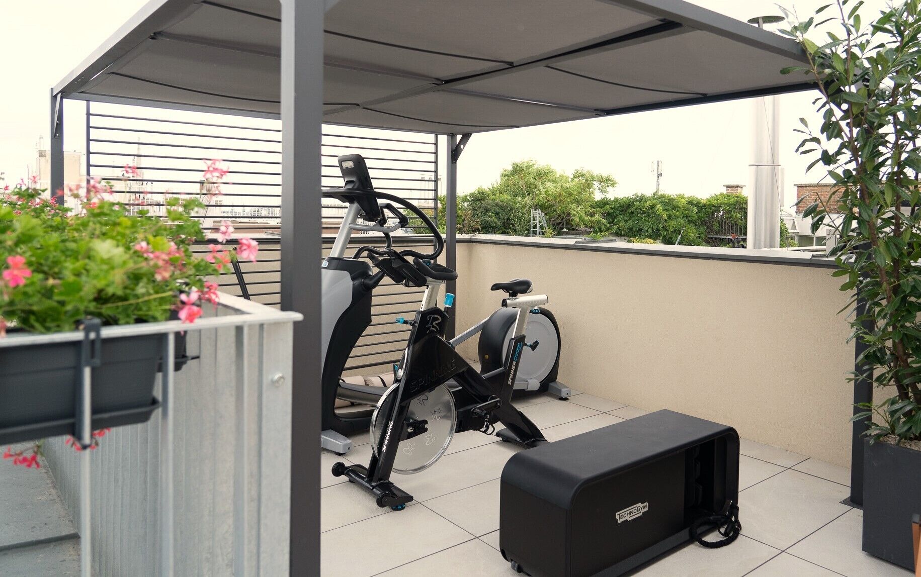 A covered outdoor area with a stationary bike, a small black speaker, and potted plants.