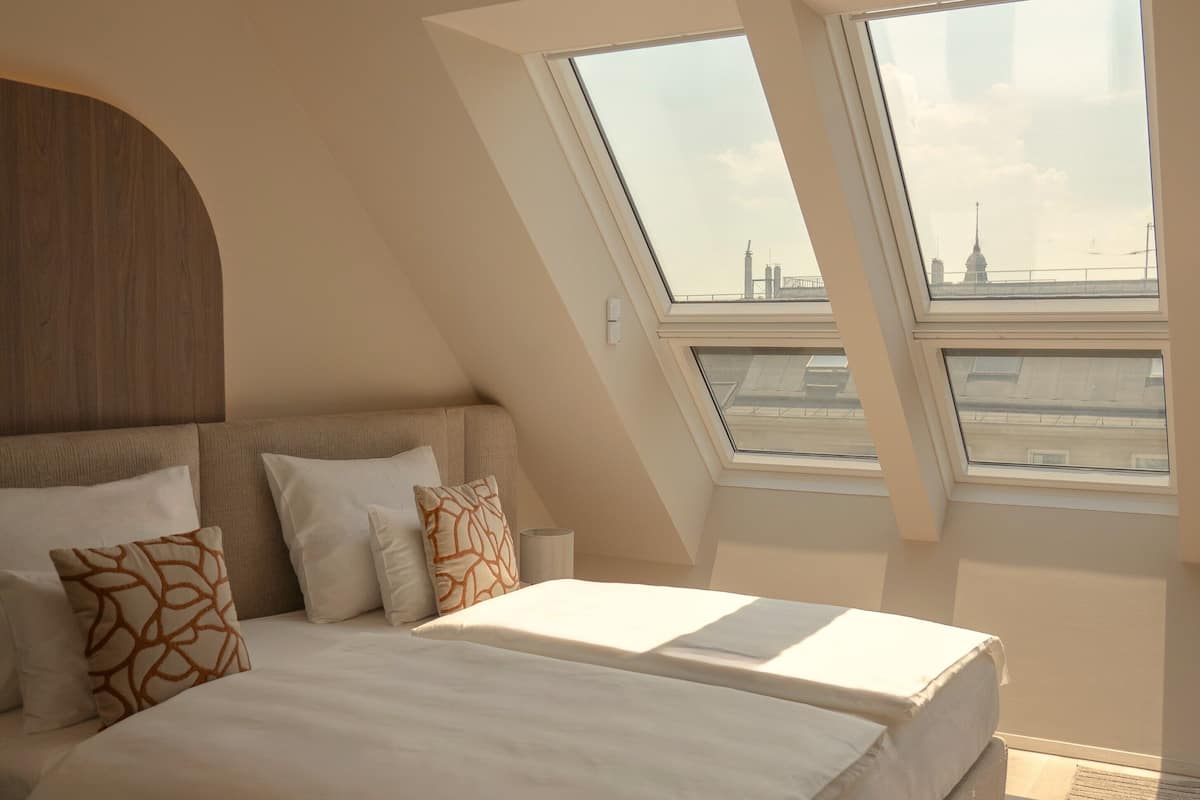 A modern bedroom with a large bed, skylight windows, and a view of the cityscape.