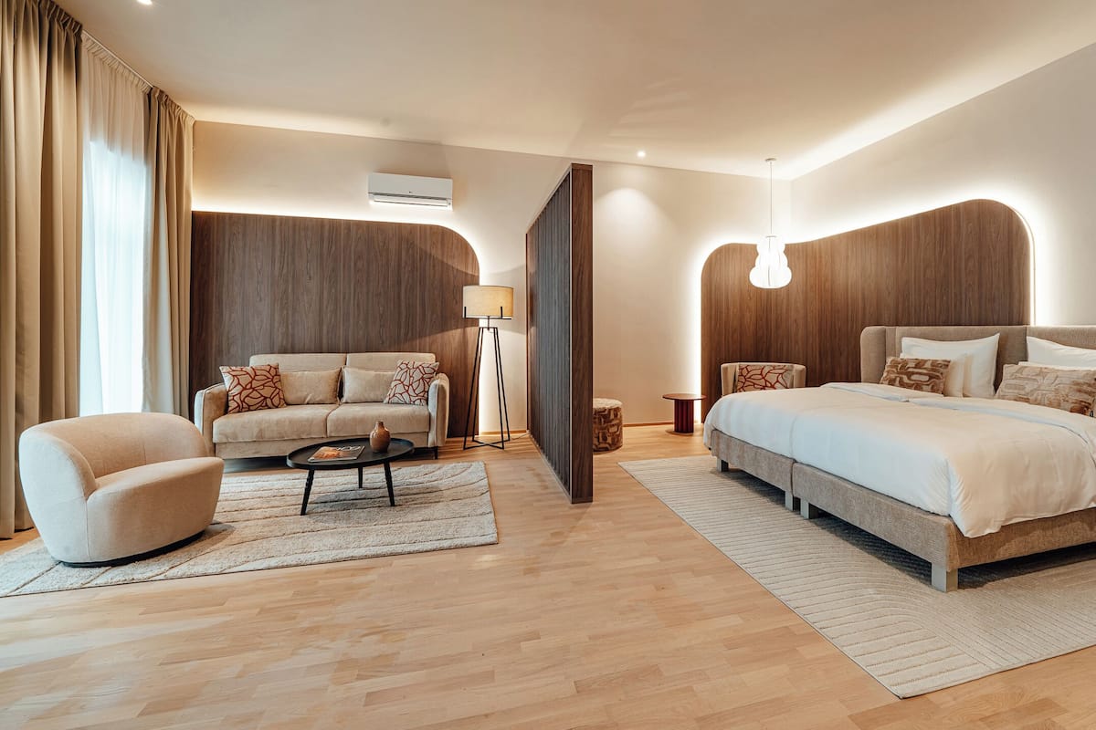 A modern hotel room with a sofa, a bed, a coffee table, and a lamp.