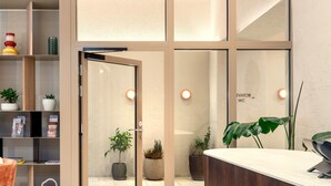 Una moderna zona de recepción con un mostrador de madera, un separador de vidrio y una planta en maceta.