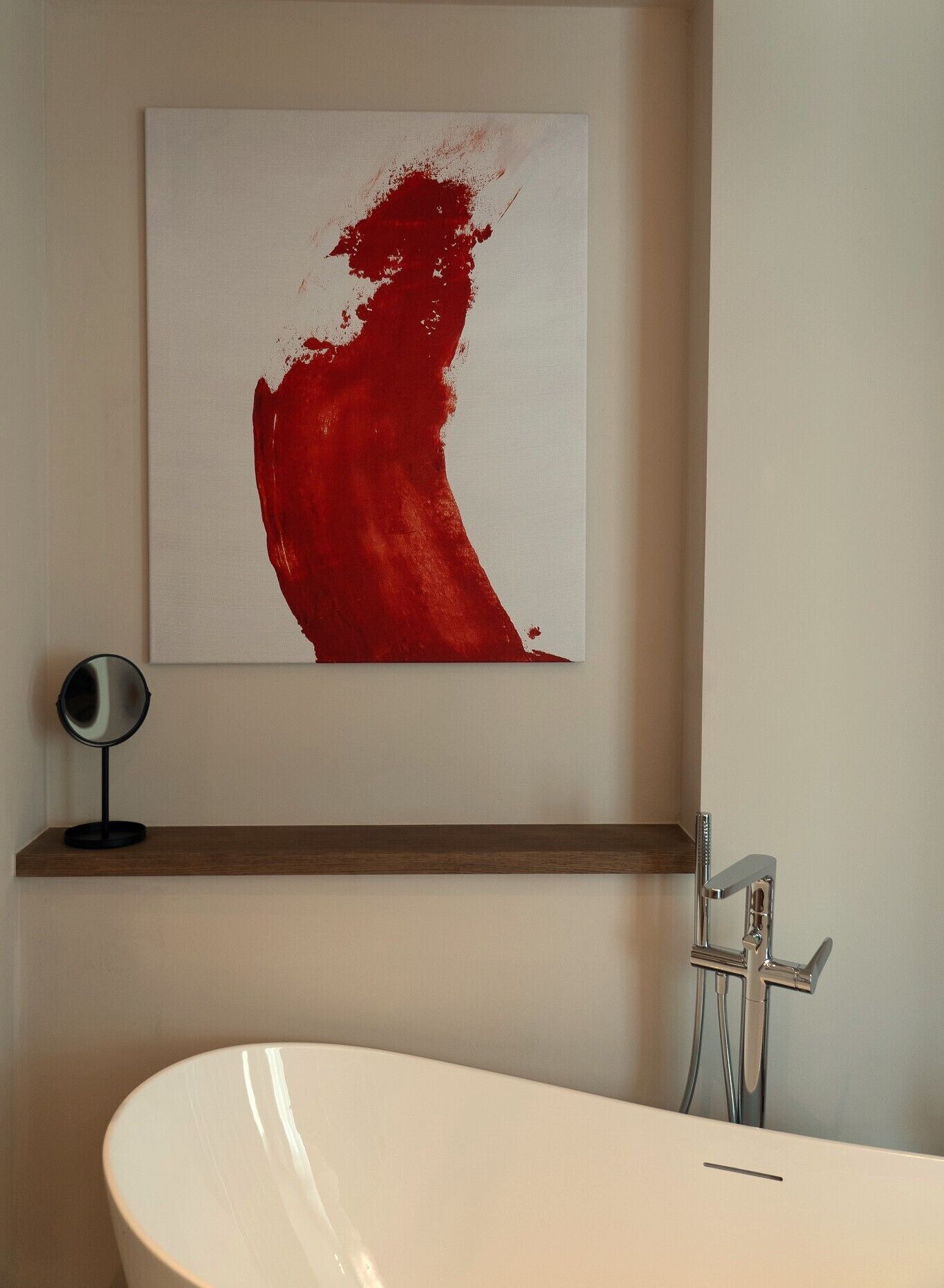 A bathroom with a white bathtub, a modern faucet, and a red abstract painting on the wall.