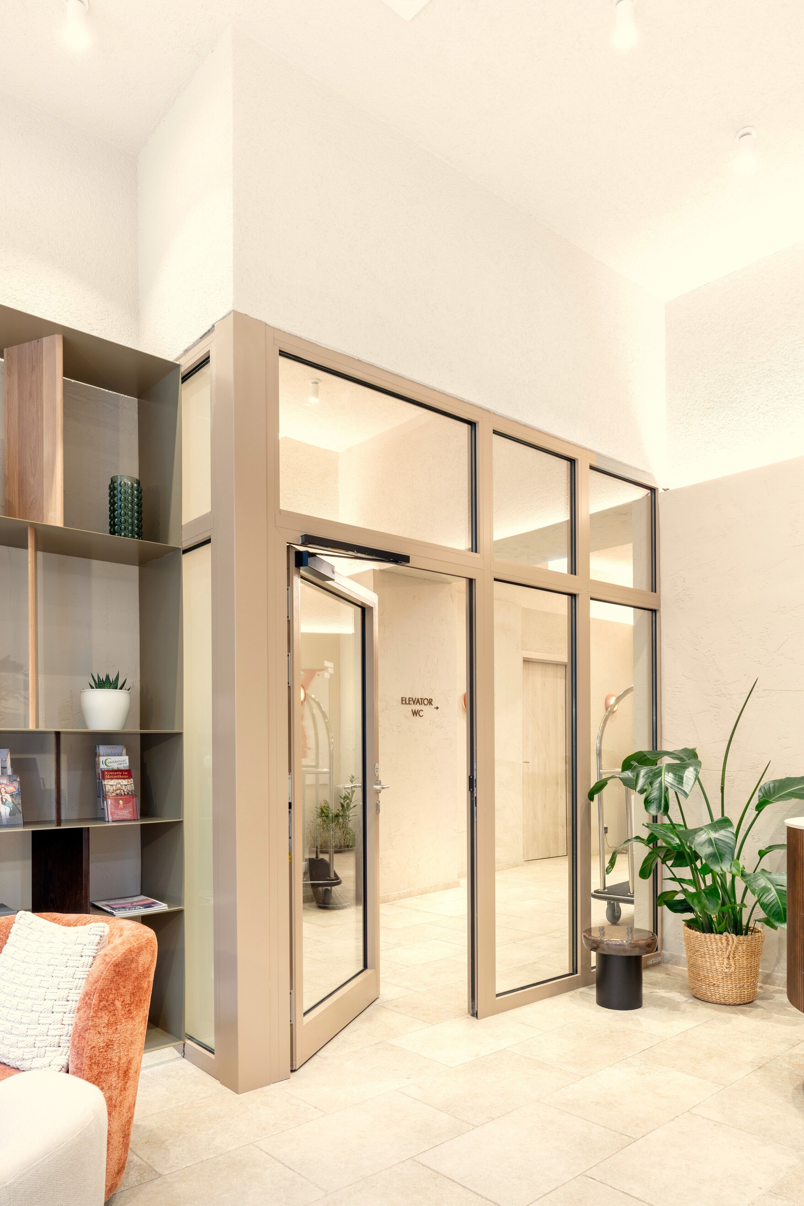 Un intérieur moderne avec une porte coulissante en verre donnant sur une salle de bain, une bibliothèque et une plante en pot.