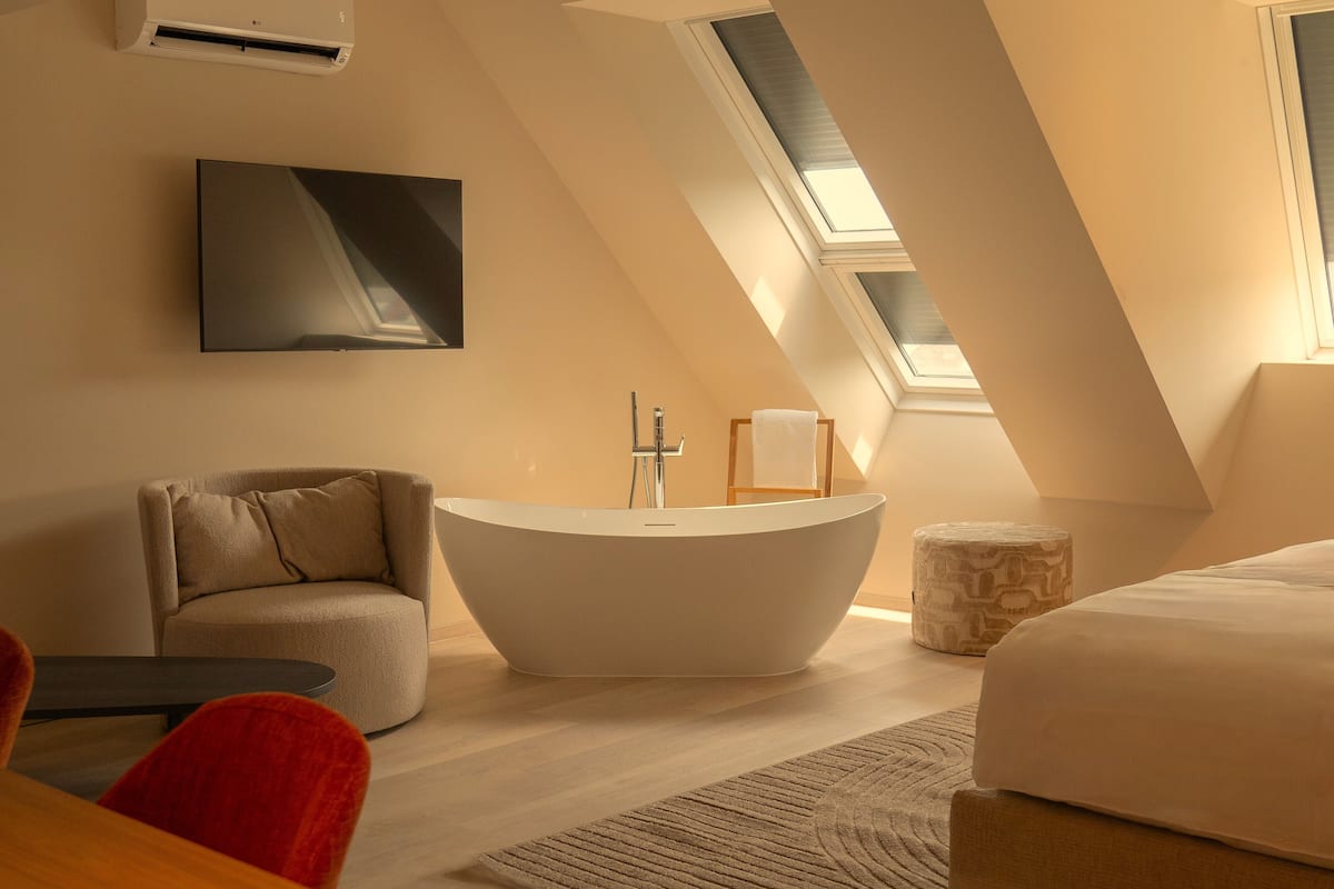 A modern bedroom with a skylight, a freestanding bathtub, a sofa, and a bed.