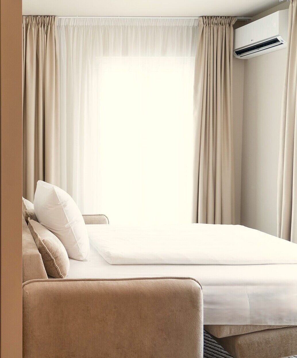 A hotel room with a bed, a sofa, and an air conditioning unit.