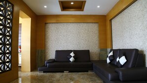 A modern lobby with two black sofas, a patterned wall, and a wooden ceiling. - Hotel Varshan International (Erode)