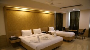 A hotel room with two beds, a desk, a chair, and a ceiling fan. - Hotel Varshan International (Erode)
