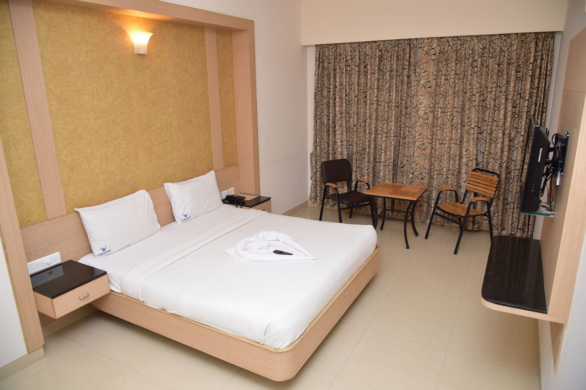 A hotel room with a bed, bedside table, lamp, desk, chairs, and a TV.