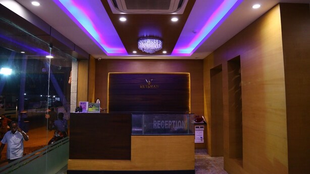A reception area with a reception desk, a chandelier, and a sign that reads "RECEPTION". - Hotel Varshan International (Erode)