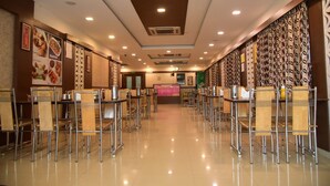 A spacious, well-lit restaurant with high tables and chairs, a central counter, and decorative wall panels. - Hotel Varshan International (Erode)