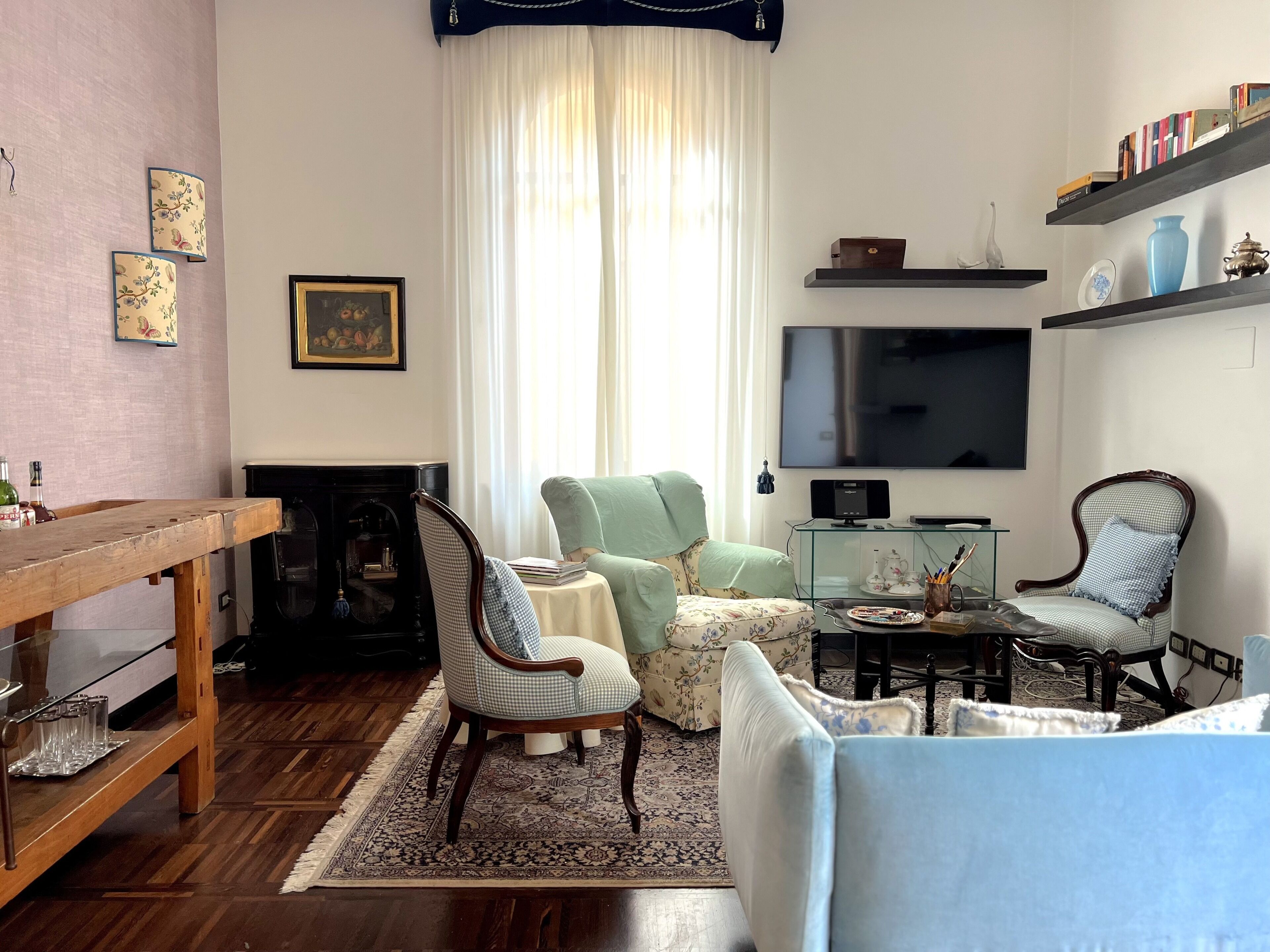 Una sala de estar con una mesa de madera, dos sillones, un sofá, una chimenea, un televisor y estantes con objetos decorativos.