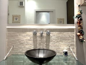 A bathroom with a glass sink, two faucets, and a mirror above. - Villa Liberty TownHouse (Siena)