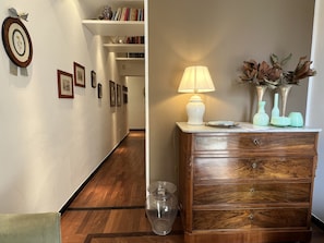 A hallway with framed pictures on the wall, a wooden floor, and a wooden dresser with a lamp and vases. - Villa Liberty TownHouse (Siena)