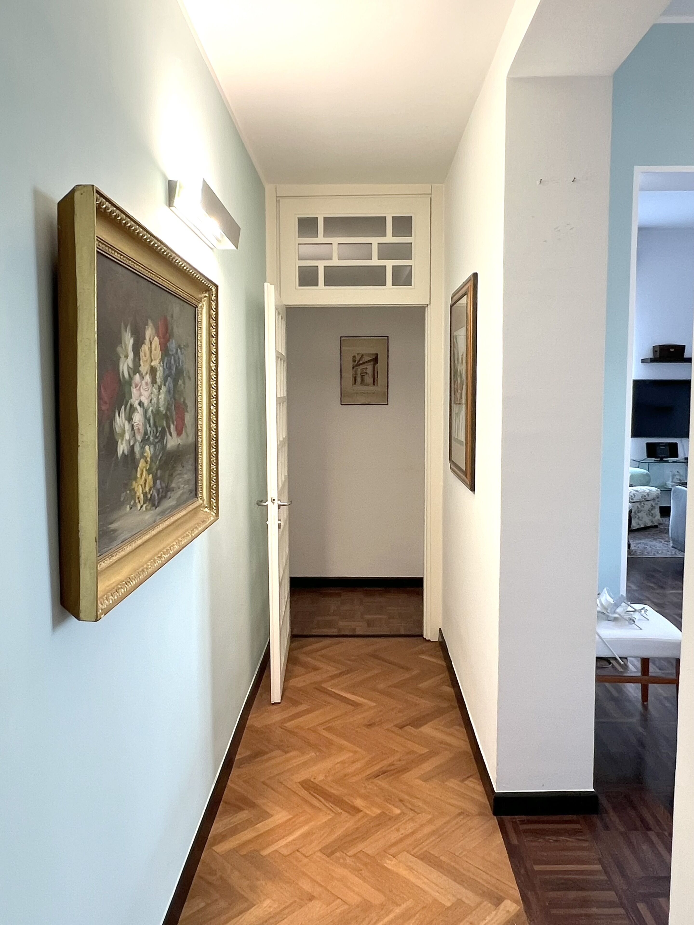 A hallway with wooden flooring, a white door, and framed artwork on the walls.