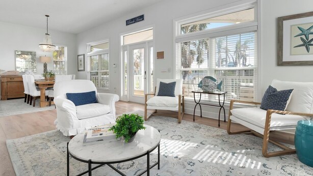 A bright, spacious living area with white furniture, large windows, and a view of palm trees.