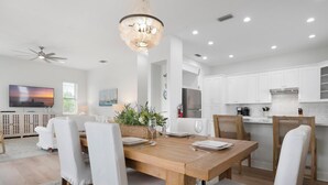 A modern kitchen with white cabinets, a wooden dining table set for four, and a chandelier.