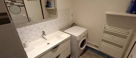 Un baño moderno con lavamanos blanco, espejo y lavadora integrada.