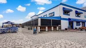 Ein Gebäude direkt am Strand mit einer blau-weißen Fassade, Außenplätzen und einem Sandstrand.