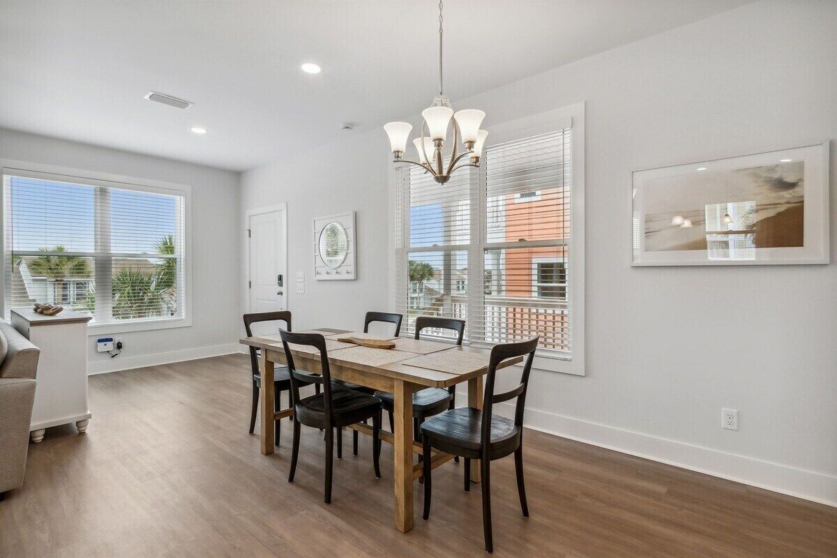 Un comedor con una mesa y sillas de madera, un candelabro y ventanas amplias con persianas.