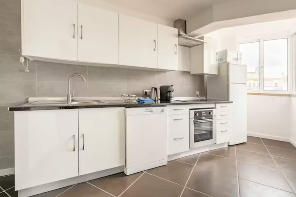 A modern kitchen with white cabinets, a stainless steel sink, a dishwasher, and an oven.