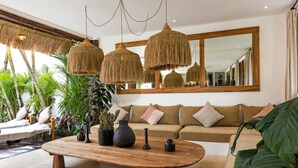 A modern living room with a wooden coffee table, hanging rattan lamps, a large mirror, and a beige sofa with cushions.